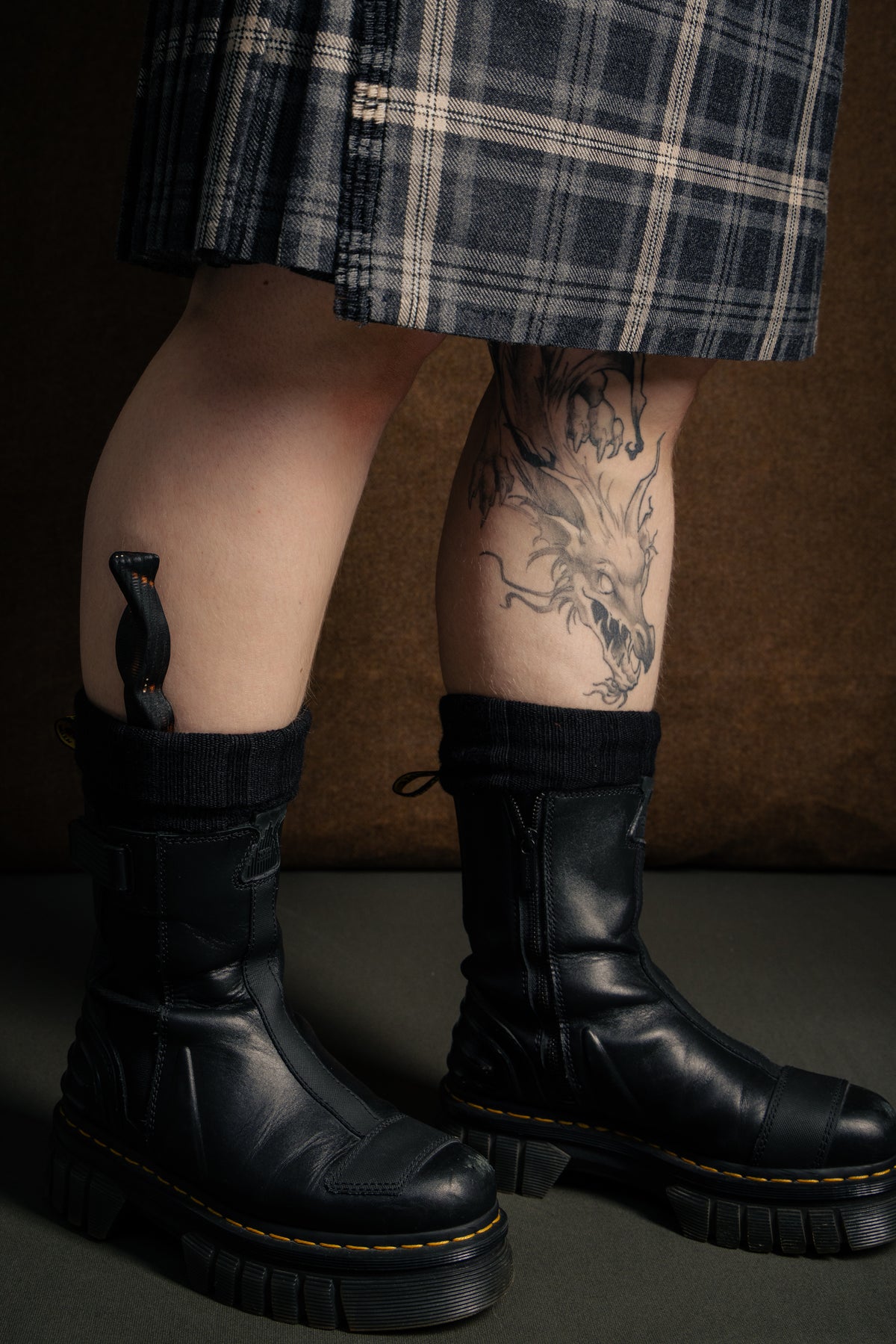 An ash wood Sgian Dubh with burned finish and silver dot inlay worn tucked in the sock with Doc Marten boots, a kilt and a dragon tattoo. 