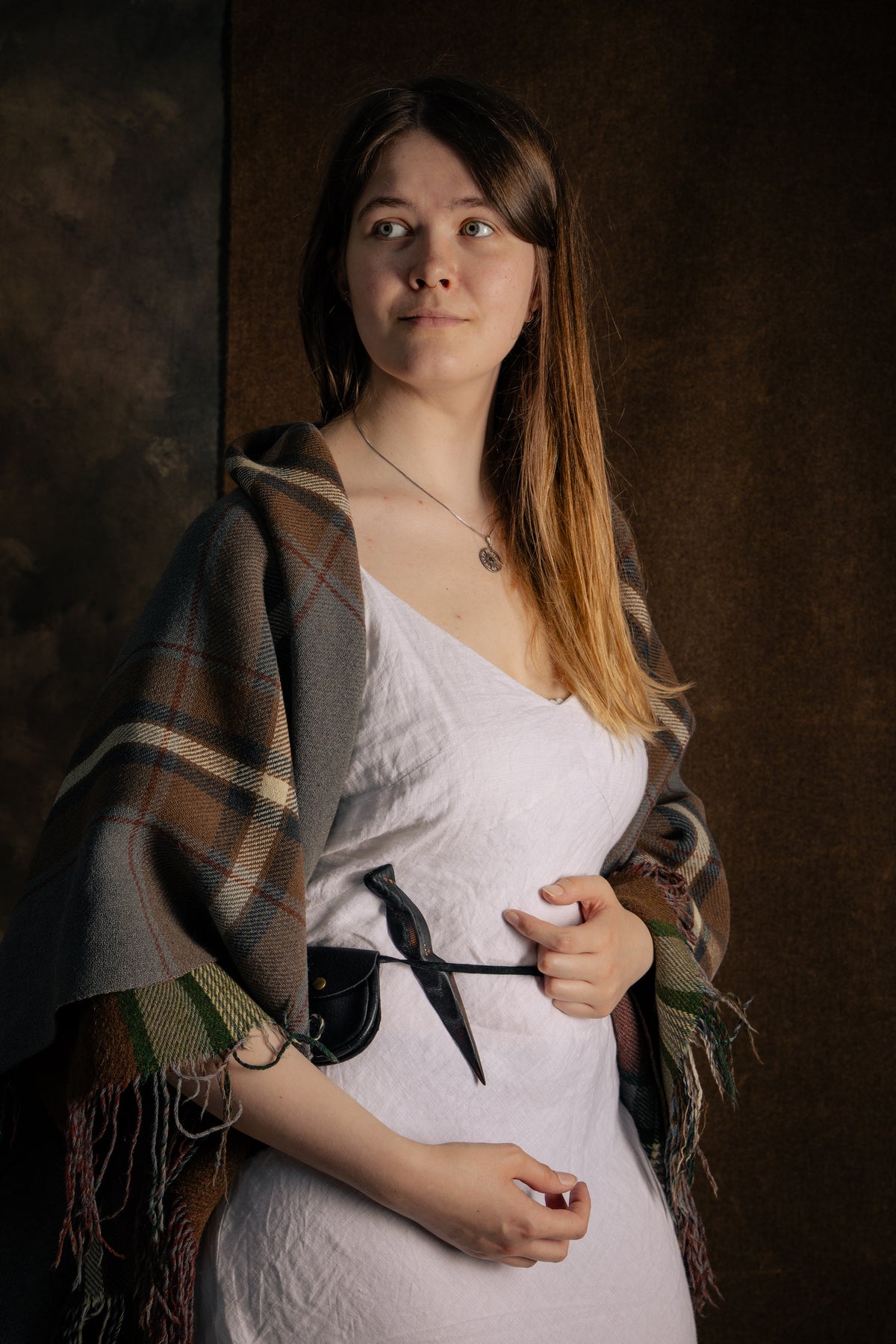 The ash wood Sgian Dubh with burned finish and silver dot inlays, worn tucked in the belt by a figure in a white dress and tartan shawl