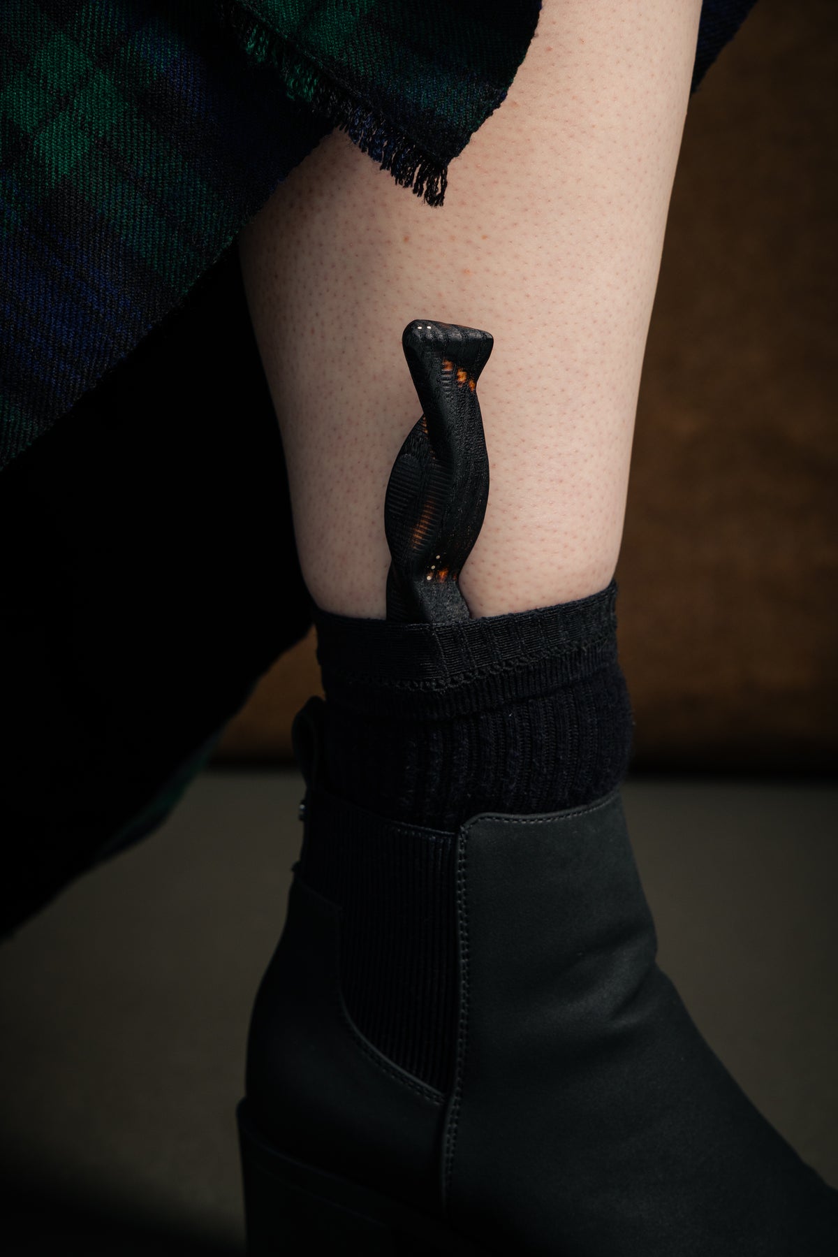 An ash wood Sgian Dubh with burned finish and silver dot inlay, worn tucked in the sock with black boots and a kilt. 